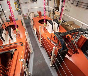 Two orange metal drop keels inside a ship suspended by winch cables