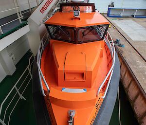 An smaller orange boat attached to the side of a ship