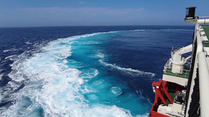 Looking out the side of a ship towards the wake caused by turning which has made the water turquoise
