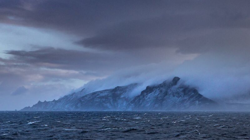 A dramatic landscape with choppy sea before an island emerges covered in low lying cloud
