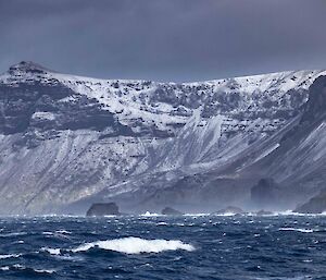 A dramatic sea scape with white snow dusted cliffs in the background