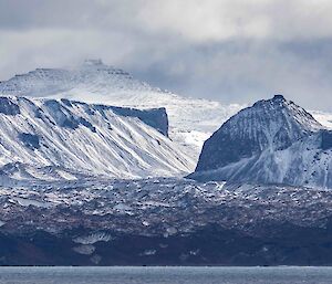 Dramatic, snow dusted cliffs and mountains rise up from the sea.  A glacier flows down towards the shore.