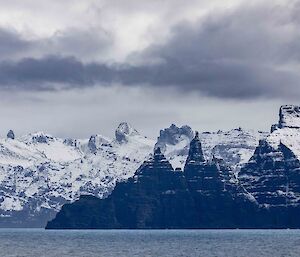 Looking from ship towards steep, dramatic cliff faces, with snowy mountains.
