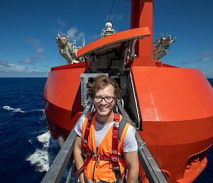 A man in a hi vis vest stands at the end of a gang plank jutting out from the front of a ship