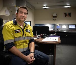 A man in hi vis sits at a desk in a control room and smiles to camera