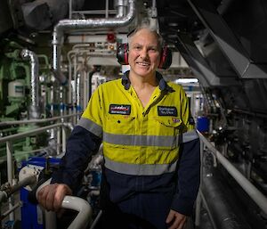 A man stands in hi-vis in the engine room of a ship smiling to camera