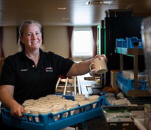A woman with a tray of mugs stands smiling to camera