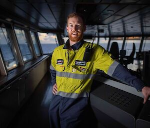 A man in hi-vis stands on the bridge of a large ship smiling to camera