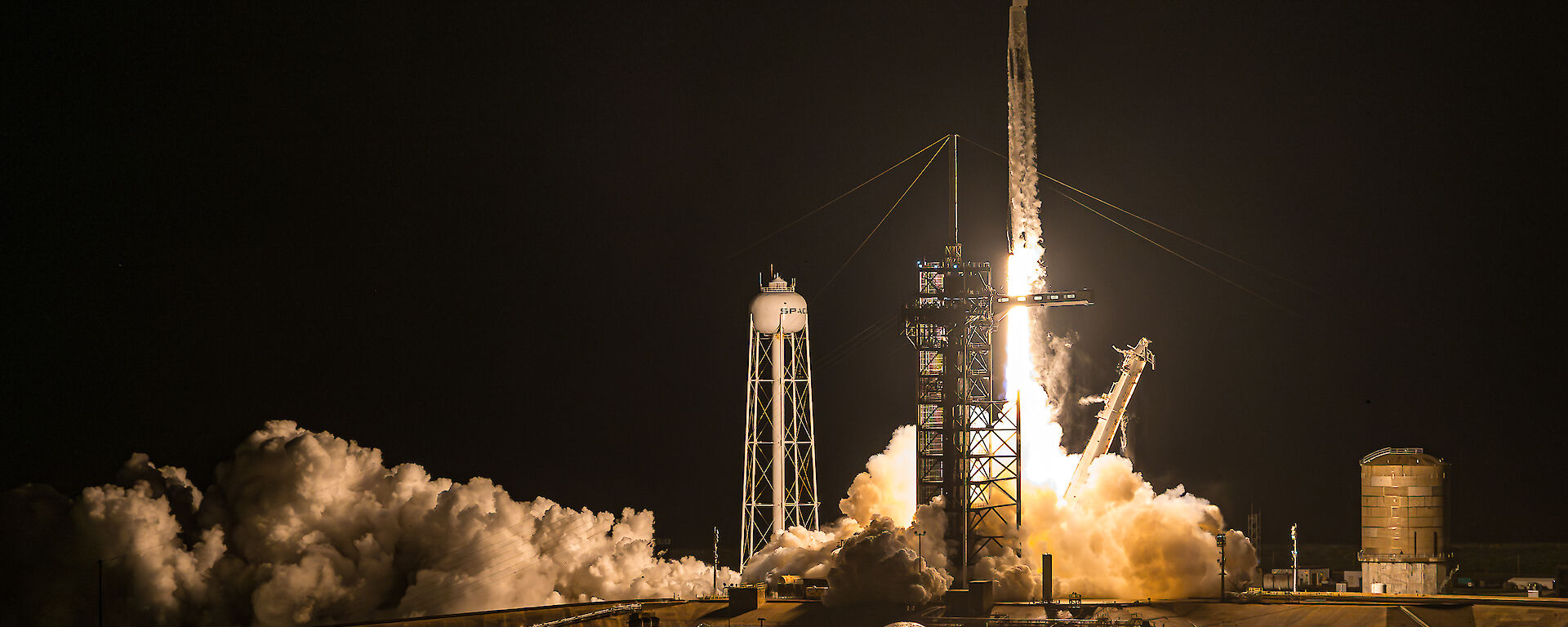 Clouds of exhaust billow around a SpaceX rocket as it launches at night.
