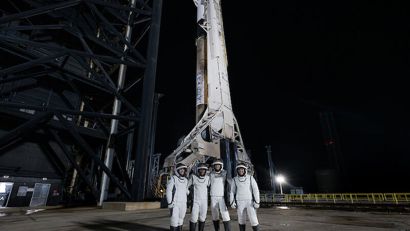 Four astronauts in white suits standing in front of a rocket at night.