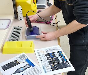 A man practices uses a hand-held ultrasound device on material designed to mimic the human body, while looking at printed instructions.