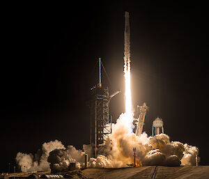 Clouds of exhaust billow around the base of a SpaceX rocket as it launches at night.