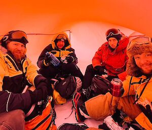 a view of 4 expeditioners within a field bivvy, a small frameless fabric shelter used to get out of the weather and have some lunch