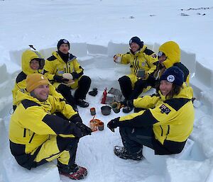 a group of 6 expeditioners captured drinking a hot chocolates inside a partially built igloo