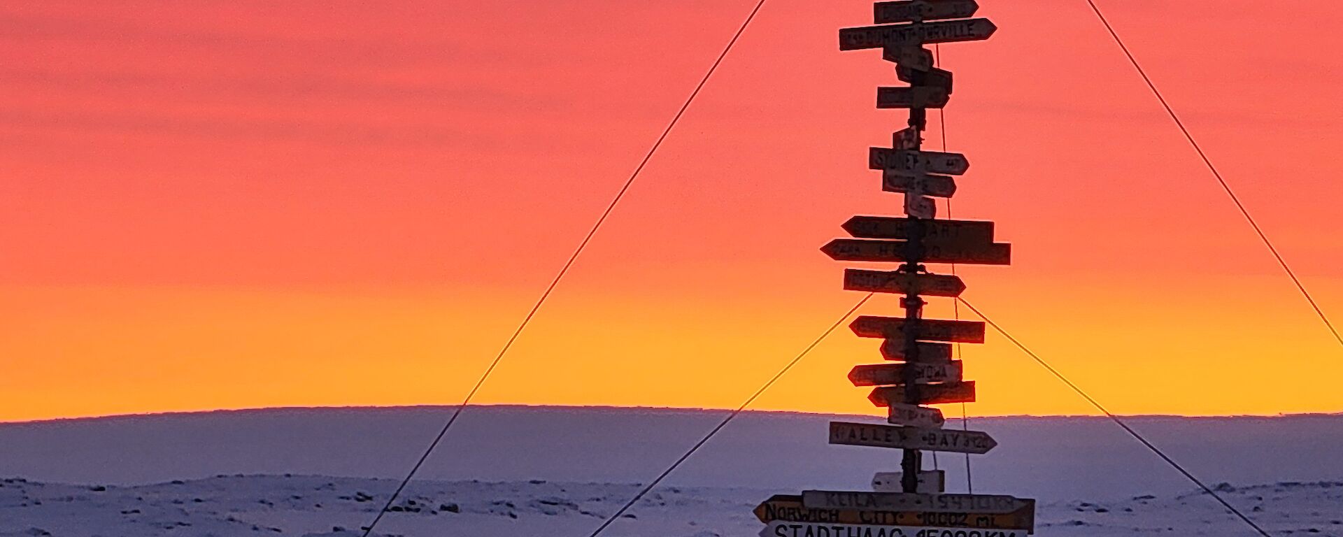 A portrait image depicting the Casey sign low lit in the foreground of backdropped background of vibrant sun arrays contrasted against a snow filled rocky outcrop