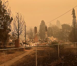 An almost monochromatic type image of a home that has burnt down, with smoke and dust creating a preternatural type effect
