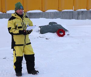 A man in yellow outdoor gear  standing on snow, reading from a speech