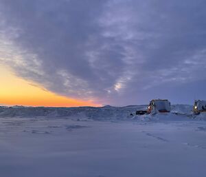 Two heavy machines in heavy snow with sunrise in the background, 2024
