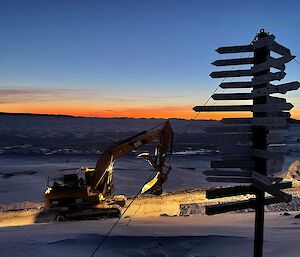 An excavator stands near the Davis signpost with twilight in the background, on snow
