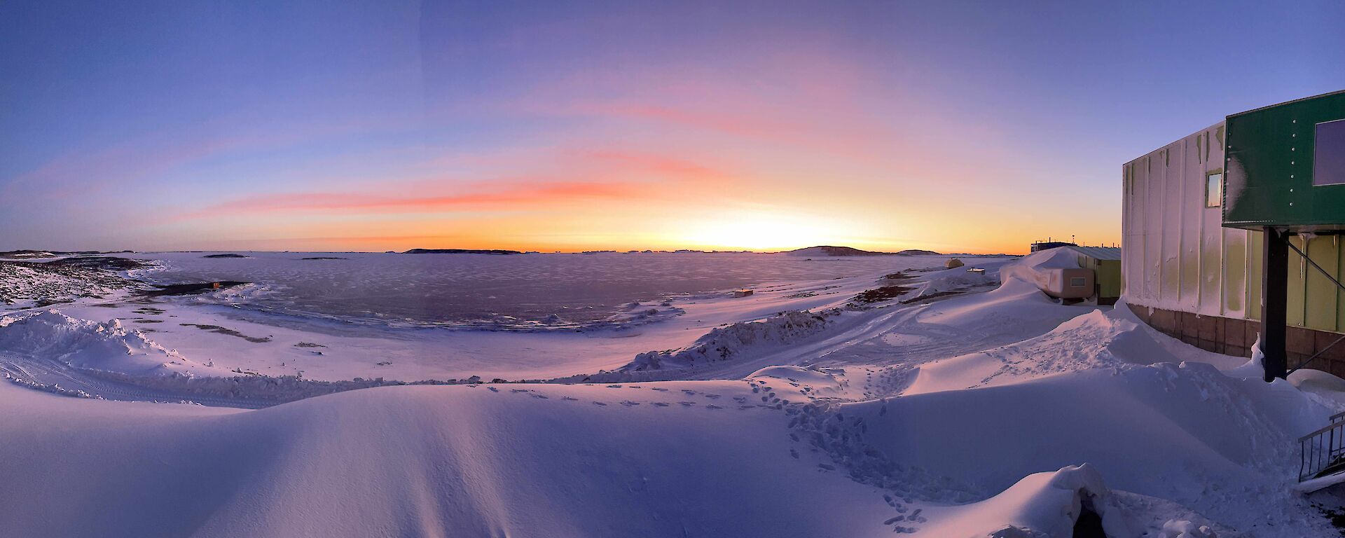 A snowy landscape with a building to the right, at twilight or dawn