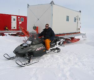 A man on a skidoo next to a shipping container on a snowy ground Casey 2003