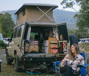 A woman sits in a camping chair near a Toyota troopcarrier with its soft top popped.