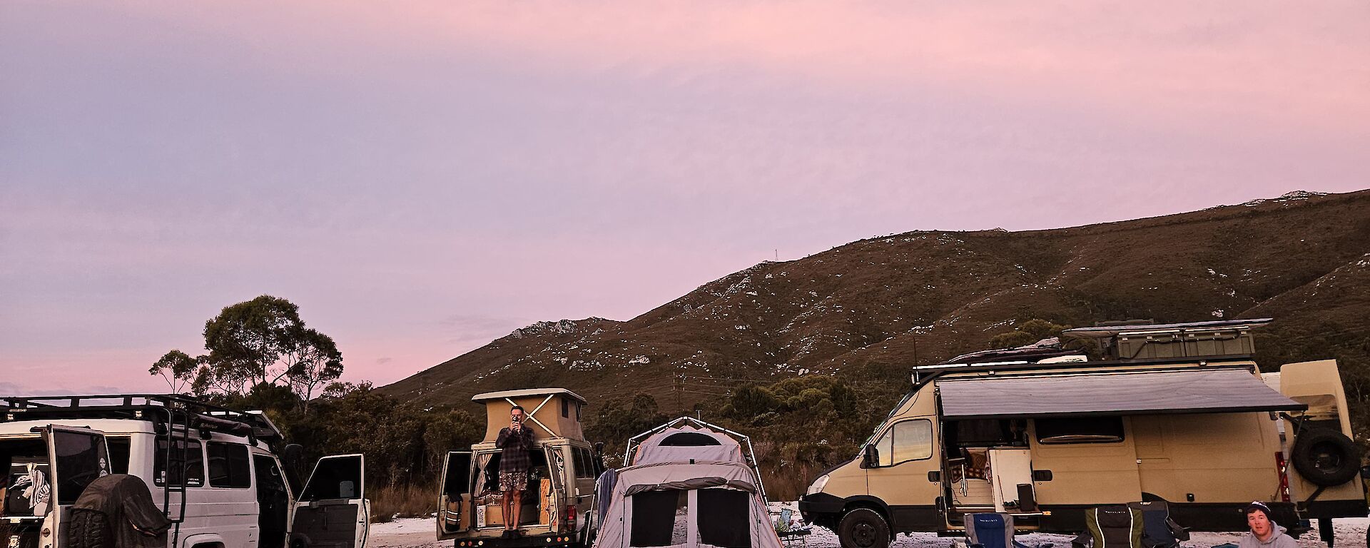 Three camper vehicles and a tent set up on white quartzite rock-covered ground with a mountain in the distance
