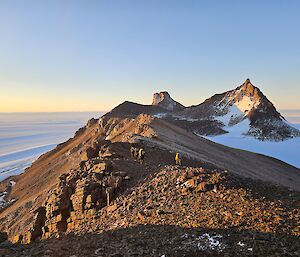Four people hiking along a rocky mountain range with the Antarctic ice below