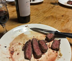 Sliced rare steak on a plate with knife on the side