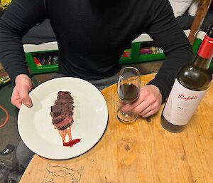 Man sitting at table holds plate of sliced steak and a glass of red wine