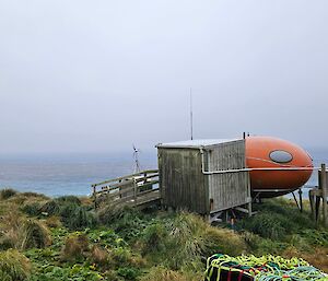 The Brother's Point Hut, a smarty hut with wooden vestibule attached. Situated on grassy slope overlooking bay.