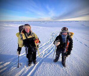 two expeditioners stand on a gradient ice slope before reaching the shoreline onto the sea ice
