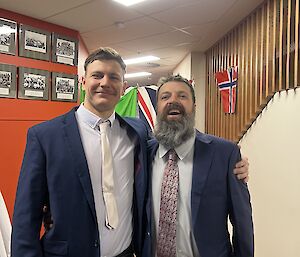 two expeditioners stand in suits with facial expressions of joy, arms around each other in a sign of camaraderie