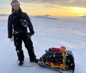 andrew is photographer with his field survival bag strapped to sled used for pulling gear onto of snow with a backdrop sunsetting silhouetted escarpments