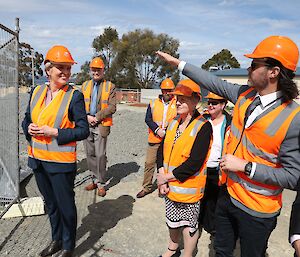Environment Minister Tanya Plibersek wearing an orange hard hat and high vis vest surrounded by six other similarly attired people, looking through a safety fence.