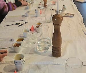A woman with a beanie on tasting a cup of soup while sitting at the white table
