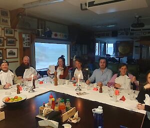 Eight people sit around a white L-shaped dining table