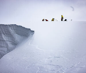 An icy cliff face with tiny people in the distance on a snowy slope