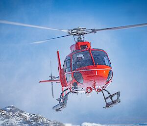 a helicopter makes its approach to land at Casey station, snow downwash surging around the engaged pilot.