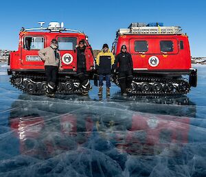 Two red Antarctic tractors stand on a frozen lake