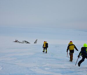The wreck of a Russian Lisunov Li2 in the plateau ice near Mawson. Three roped up expeditoners are walking towards the wreck