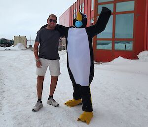 Expeditioner Terry stands happily next to a person in a penguin costume outside Casey Redshed upon arrival.