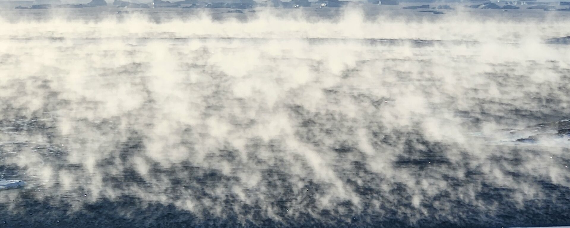 A landscape image depicting a snow shore line meeting cold water convection, a weather phenomena in-which visible moisture evaporates from the ocean. Newcomb Bay - Casey Station