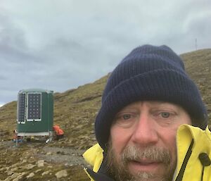 Selfie of man with small watertank hut with solar panels on the side