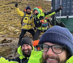 Another selfie, four people celebrating outside the watertank hut with solar panels on side