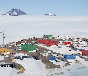 A colourful collection of buildings sitting in an ice-free area below the Antarctic plateau, with rocky mountain peaks in the distance.