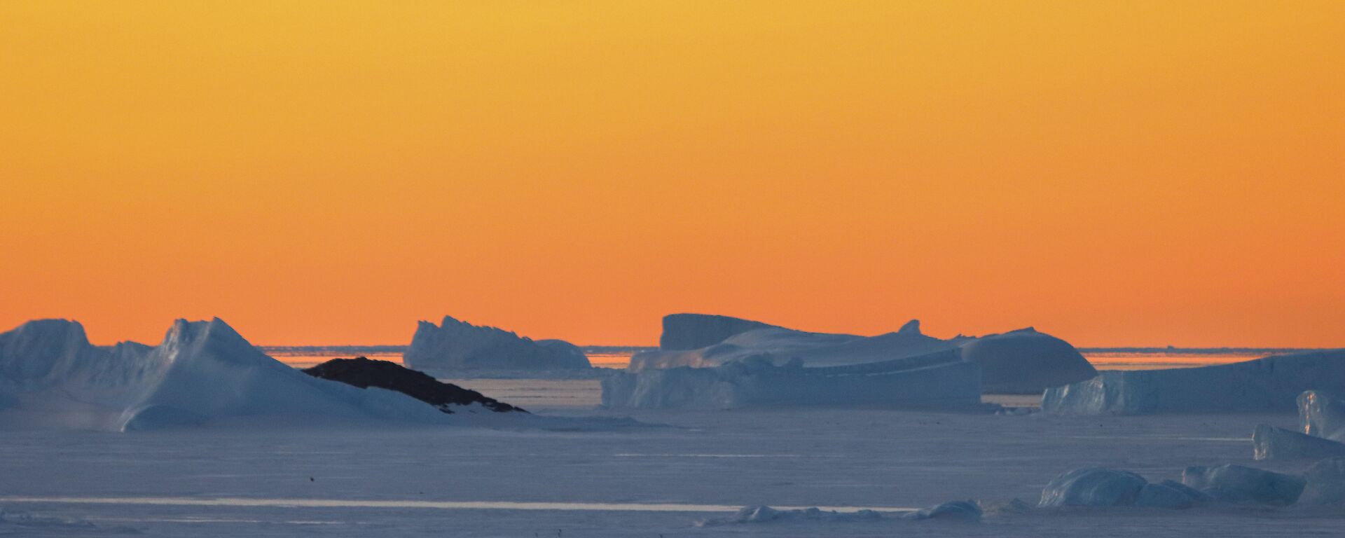 An orange-sky sunset over icebergs