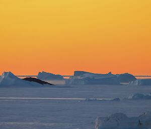 An orange-sky sunset over icebergs