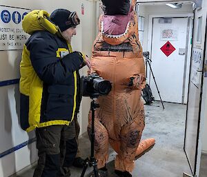 A view of a blow up dinosaur costume actor receiving guidance by Station leader dave before a filmed scene.