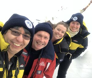 A selfie of four people in warm weather clothing standing in a line behind each other.